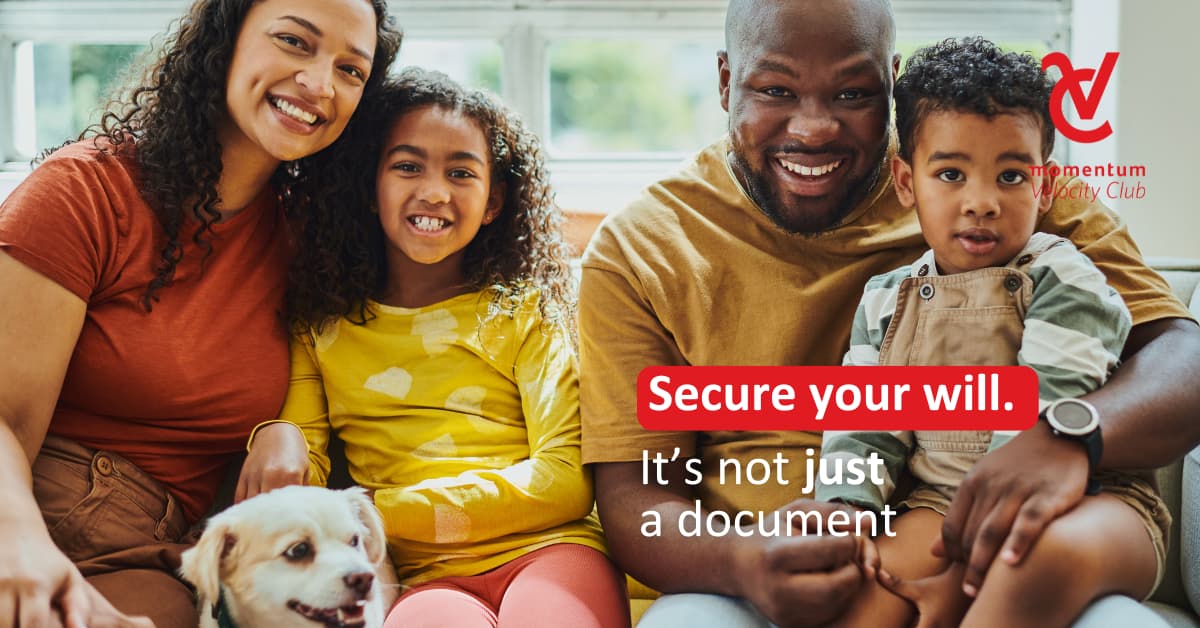 A mom and dad seated with their two young children on a couch. Next to the mom is a white dog sitting on the floor.