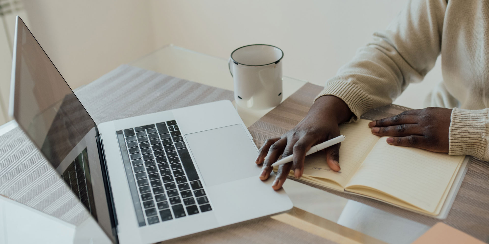 A person seated at their desk. On the desk are their notebook and laptop.
