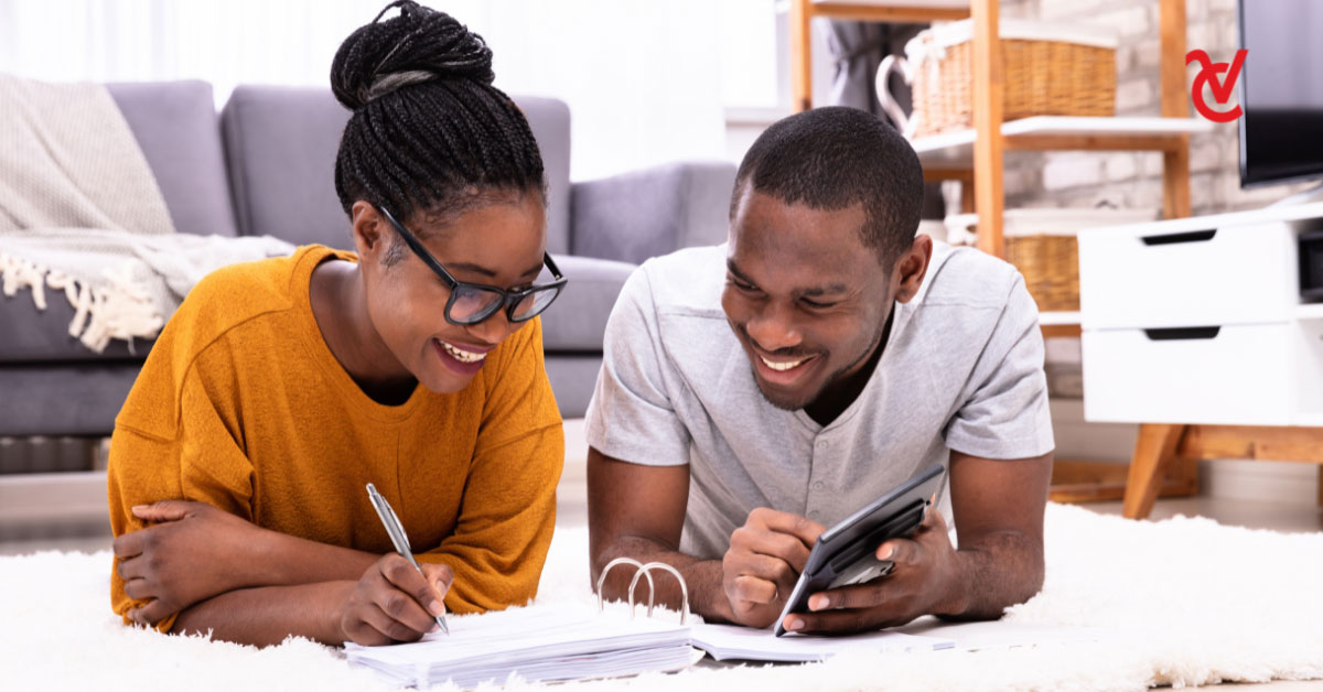 A young man and woman lying on their stomachs in their living room while they review their finances.