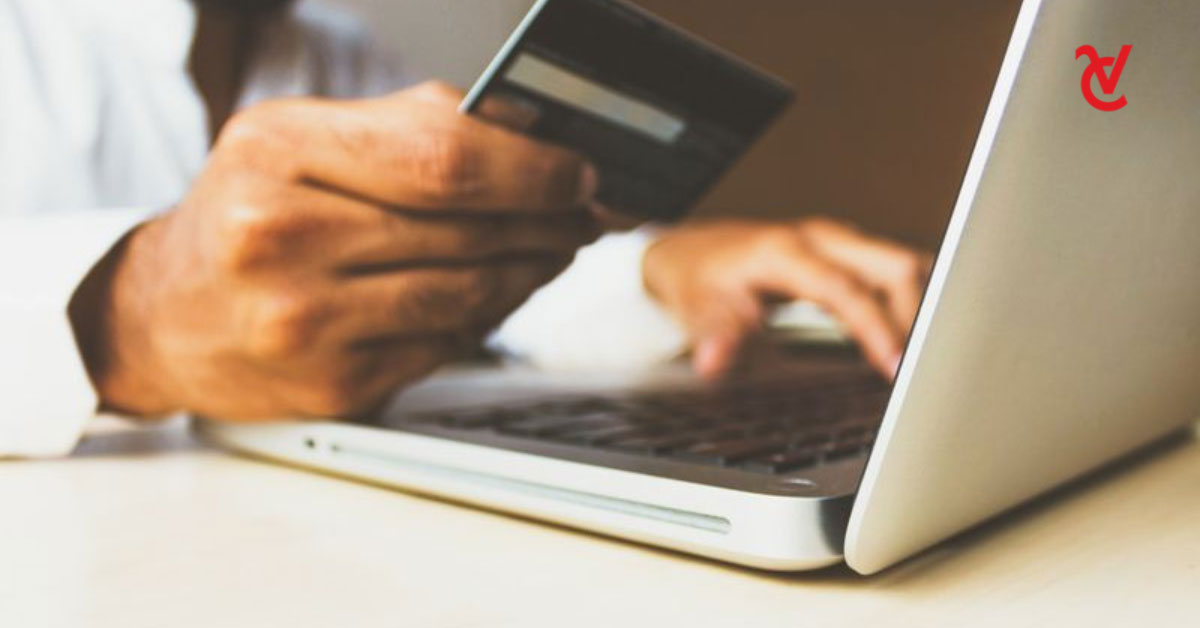 A man holding his bank card in one hand and typing on his laptop with his other hand.