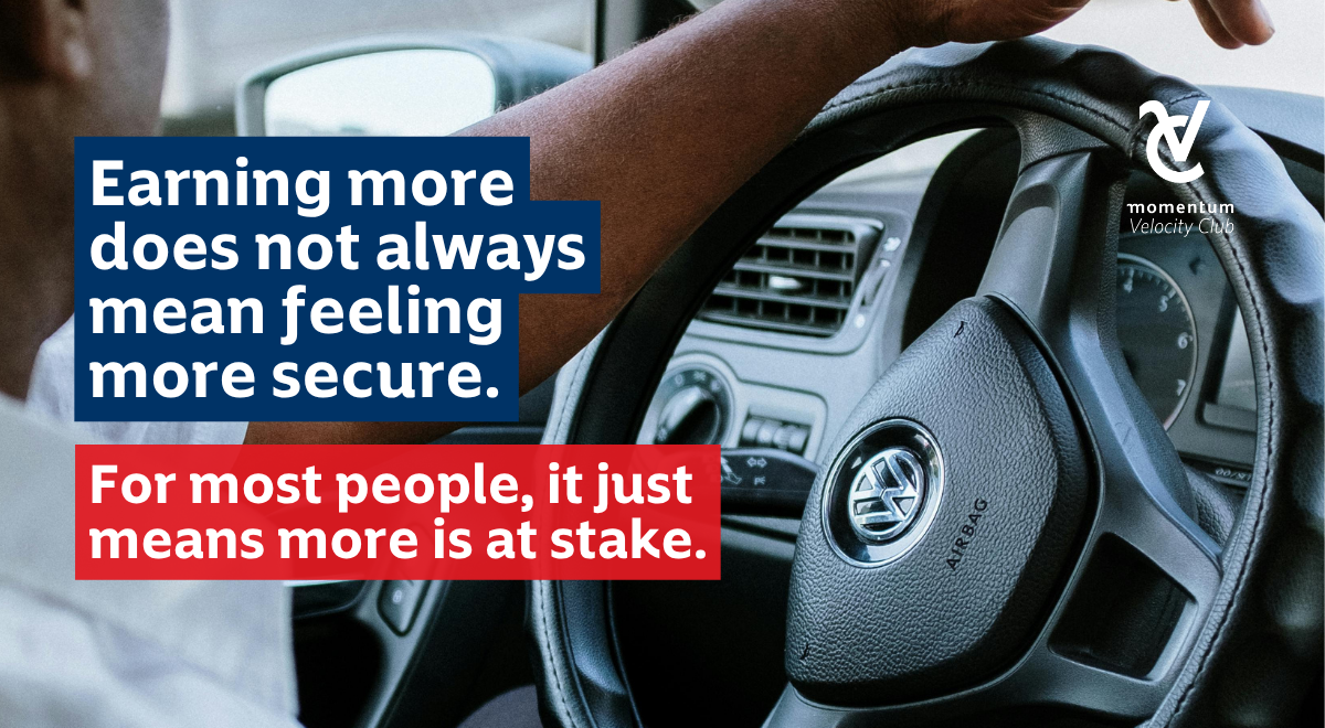 A close-up of a hand on a Volkswagen steering wheel, symbolising how earning more doesn&rsquo;t always bring security, often, it just means more is at stake. Momentum Velocity Club logo is on the top right.