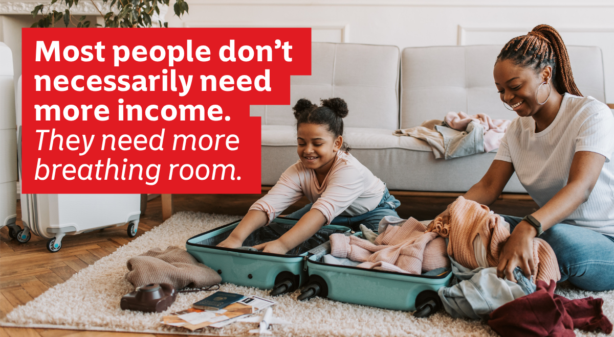 A woman and her daughter preparing to travel, happily pack open suitcases in their living room, representing a moment of "breathing room" made possible by financial stability.