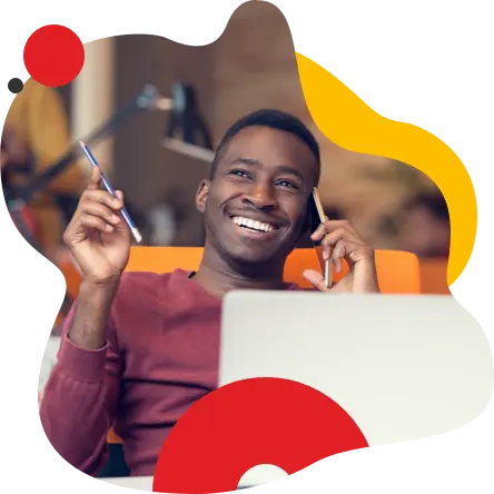 Young man smiles while talking on his cell phone and holding a pencil in his other hand.