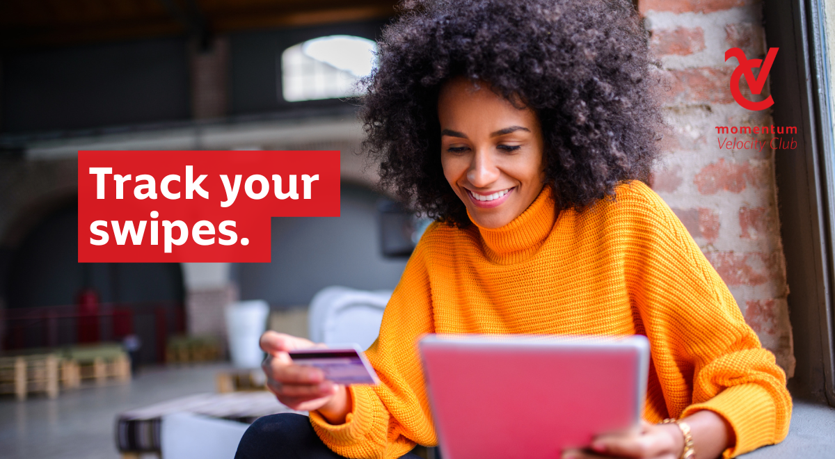 A woman sits with her credit card and laptop, reviewing her bank statement to check her card swipes.